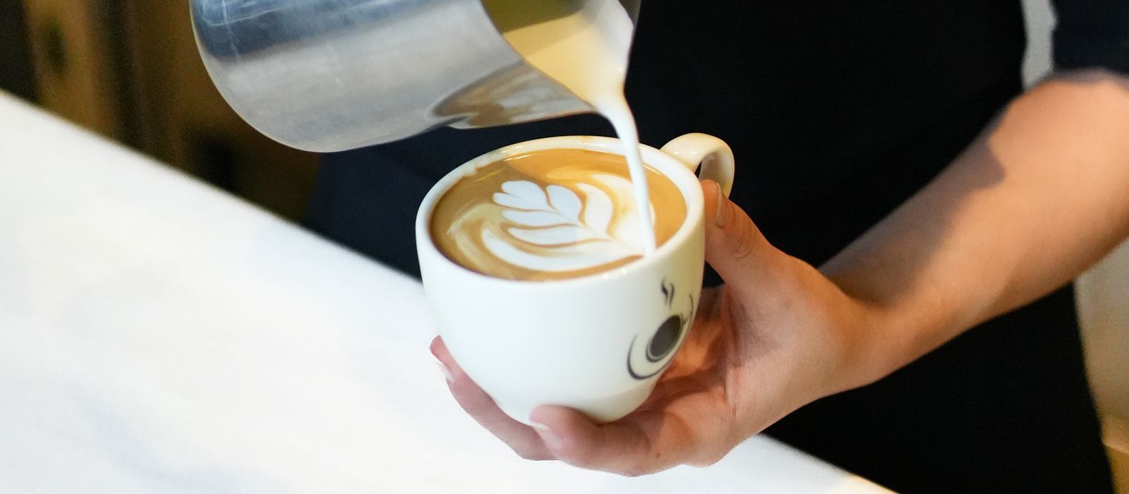 A barista pouring steamed milk into a cup, forming a rosetta latte art