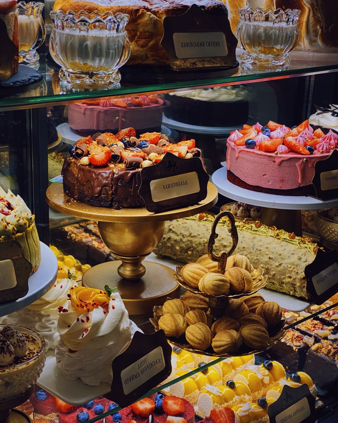 A glass display case full of layered cakes topped with strawberries, chocolate curls and meringue